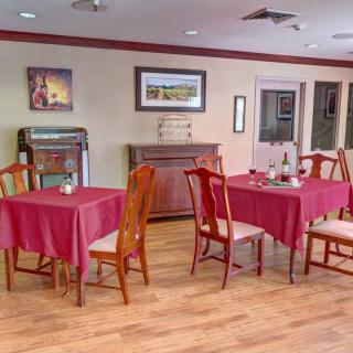 A cozy dining room with red tablecloths and wooden chairs, featuring artwork on the walls and a jukebox.