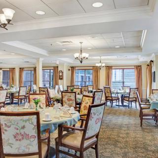 An elegant dining room with tables and chairs neatly arranged, featuring chandeliers and large windows.