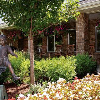 A beautifully landscaped garden with a statue, colorful flowers, and a brick building in the background.