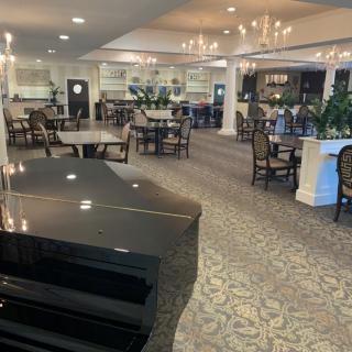 A spacious and elegant restaurant dining area featuring a grand piano and chandeliers.