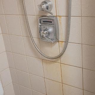 A close-up view of a shower setup, highlighting water stains on the tiles and the shower controls.