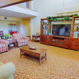 A cozy living room featuring a large entertainment center with a television, accompanied by striped chairs and a wooden coffee table.