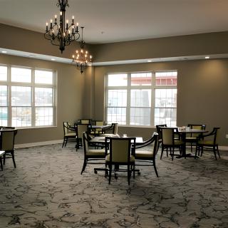 A spacious dining room with multiple tables and chairs, featuring large windows and a chandelier.