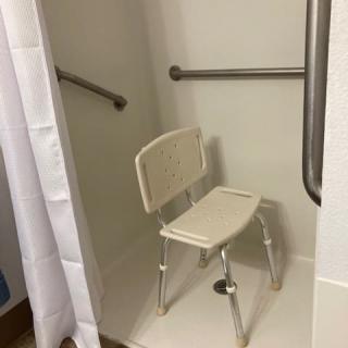 A bathroom shower with a safety chair and grab bars for accessibility.