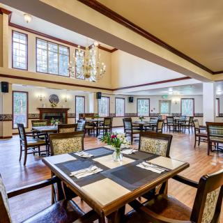 Elegant dining area with stylish furniture and chandeliers, featuring large windows and wooden floors.