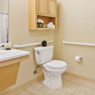 A clean and accessible bathroom with handrails, a toilet, sink, and storage cabinet.