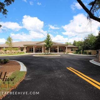 A scenic view of a building entrance with a curved driveway, surrounded by trees under a partly cloudy sky.