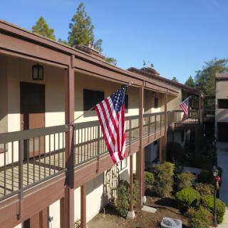 An American flag displayed on a balcony of an apartment complex under a clear blue sky.
