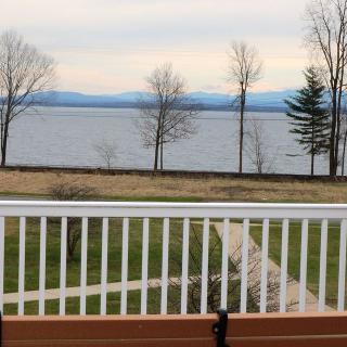 A serene view of a lake with trees and distant mountains visible from behind a fence.