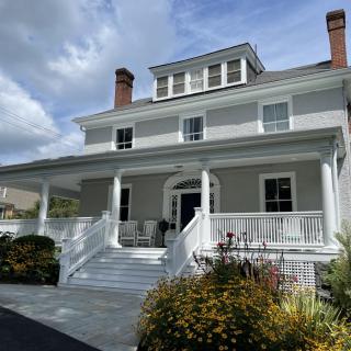 A large white house with a spacious porch and surrounding garden under a partly cloudy sky.