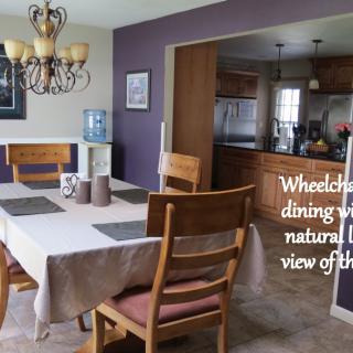 A wheelchair accessible dining room with natural light and a view of the kitchen.