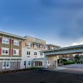 A modern healthcare facility with an extended covered driveway and a cloudy sky backdrop.