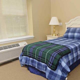 A cozy bedroom with a single bed and plaid bedding next to a nightstand and lamp.