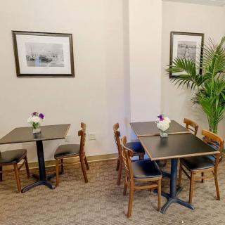 A cozy cafe interior with tables and chairs arranged neatly, adorned with framed artwork and a potted plant.