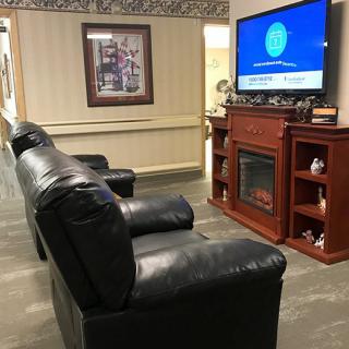 A cozy living room setup with armchairs facing a television and an electric fireplace.