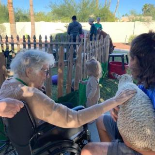A family interacting outdoors, with one person in a wheelchair and a child nearby, next to a wooden fence.
