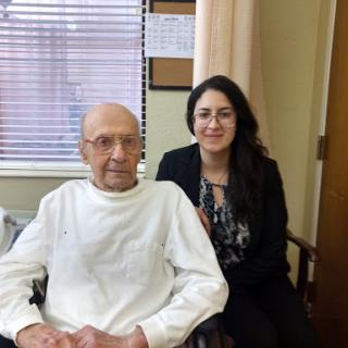 A caregiver poses for a photo with an elderly man in a hospital setting.