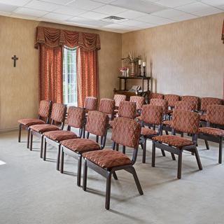 A small, intimate room set up with rows of chairs and a shelf decorated with candles.