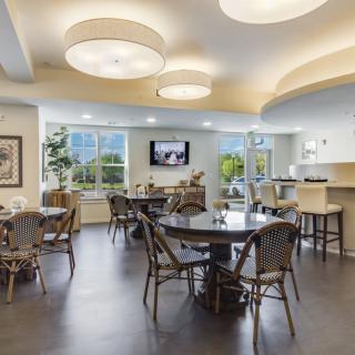 A modern dining area with tables and chairs, featuring large windows and contemporary lighting.