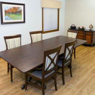 A dining room with a wooden table and six chairs, featuring a wooden floor and wall art.
