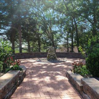 A peaceful garden with a brick pathway leading to a stone structure surrounded by trees.