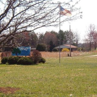 An outdoor scene with a sign, U.S. flag, and building amidst grassy surroundings.