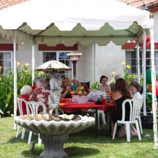 A group of people enjoying an outdoor gathering under a white tent in a garden setting.