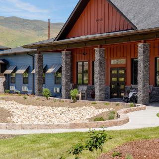 A modern building with stone pillars and landscaped surroundings against a mountainous backdrop.
