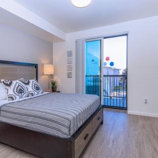 A modern and minimalist bedroom with a large bed, bedside lamp, and window leading to a balcony.