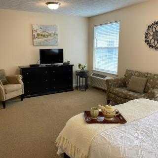 A cozy, modern bedroom with a bed, TV, armchairs, and wall decor.