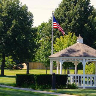 A serene park with a gazebo and American flag surrounded by lush trees.