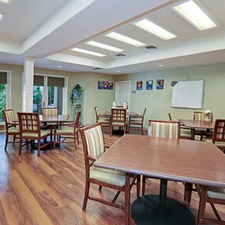 A communal dining area with wooden floors and multiple tables and chairs.