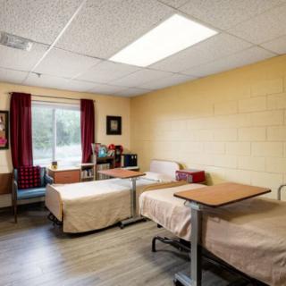 A hospital room with two beds, tables, and a window with curtains.