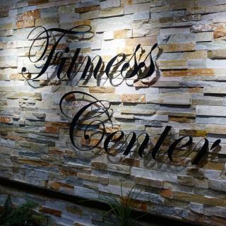 A stylishly illuminated 'Fitness Center' sign on a stone wall.