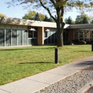 A modern building exterior with large windows, surrounded by a well-kept lawn and trees.