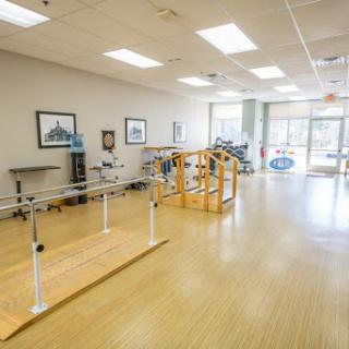 A well-lit physical therapy room equipped with walking bars and rehabilitation tools.