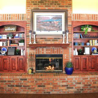 A cozy living room with a brick fireplace flanked by built-in bookshelves and decorated with artwork above.