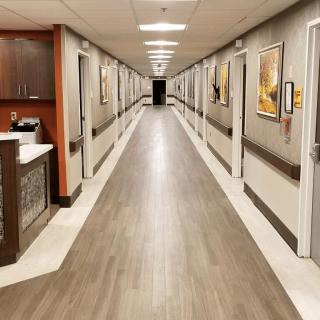 A well-lit hospital corridor featuring multiple doors and framed artwork on the walls.