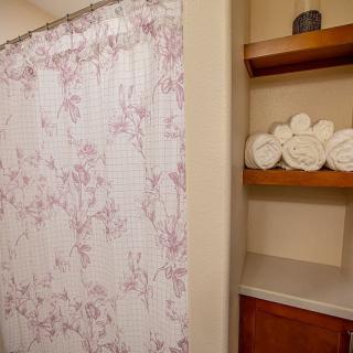 A bathroom with a floral shower curtain and neatly arranged towels on shelves.