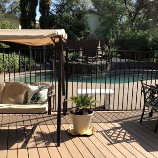A sunny patio with a swing and potted plants next to a fenced swimming pool.