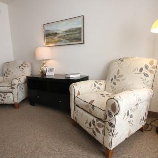 A cozy living room setup featuring two floral armchairs, a side table with a lamp, and wall art.