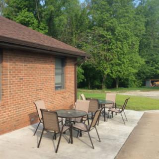 A patio with outdoor furniture next to a brick building surrounded by greenery.