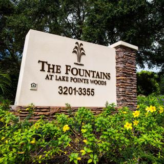 Entrance sign for The Fountains at Lake Pointe Woods surrounded by greenery and flowers.