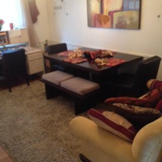 A cozy dining room with a dark wooden table, chairs, and a bench, accented by a plush rug and wall artwork.