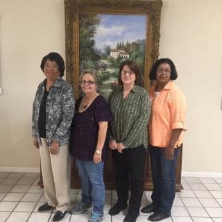 A group of four people standing indoors in front of a framed painting.