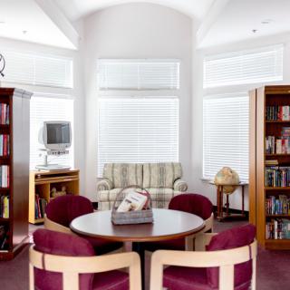 A cozy library with a round table and chairs, surrounded by bookshelves and a sofa.