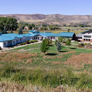 Aerial view of a complex with blue roofs surrounded by grassy fields and mountains in the background.