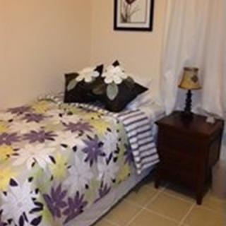 A cozy bedroom featuring a single bed with floral bedding, complemented by a wooden nightstand and lamp.
