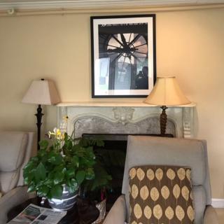 A cozy living room setup featuring armchairs, lamps on either side of a fireplace, a framed artwork above, and a plant on the table.