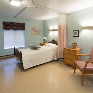 A well-lit hospital room featuring a single bed, bedside table, and a comfortable chair.